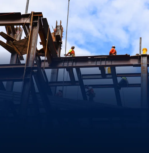 Workers in orange safety vests and helmets standing on steel beams at a construction site