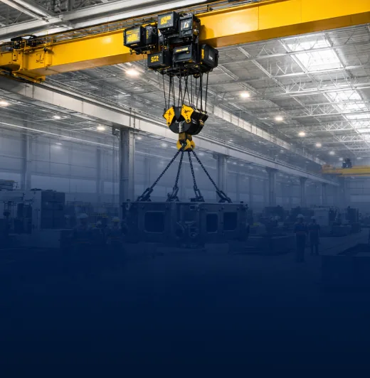 Yellow overhead crane with multi-chain hook assembly lifting load inside a factory